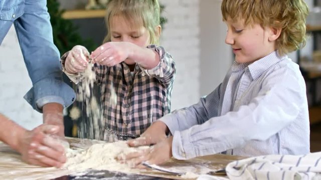 Medium shot of two children of primary school age and their unrecognizable father spreading flour on kitchen worktop