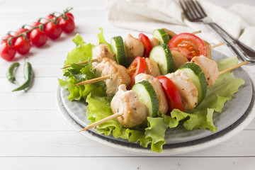 Traditional chicken kebab on wooden skewers with tomatoes, cucumbers and fresh herbs on a plate.