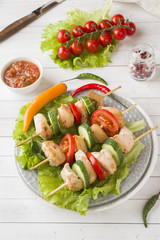 Traditional chicken kebab on wooden skewers with tomatoes, cucumbers and fresh herbs on a plate.