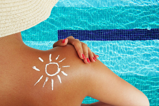 Young woman protecting her skin with sun lotion at the swimming pool, back view of an unrecognisable person
