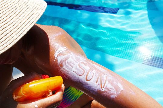 Attractive woman protecting her skin against sunburn or sunstroke, applying sun lotion on the poolside
