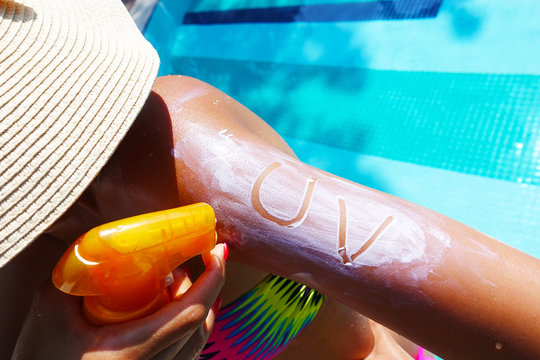 Ultraviolet protection concept with UV text on sunscreen on young woman arm at the swimming pool 
