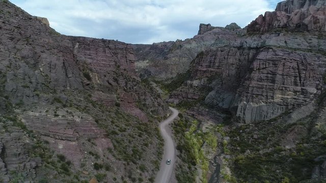 Aerial drone scene of Atuel river Canyon in San Rafael, Mendoza, Cuyo Argentina. Camera moving forwards tracking modern new 4x4 van. Gravel street next trees and river. Colorfull rocks.