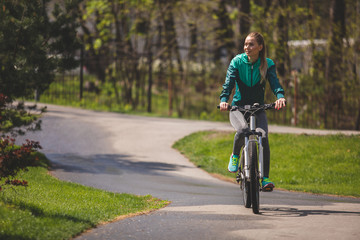 Happy calm lady is riding bike along path outdoors. She is looking at nice green nature around her. Copy space in left side