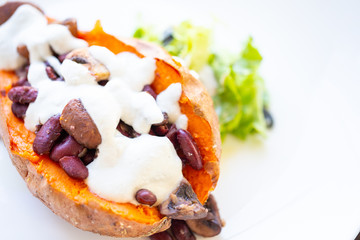 Closeup of vegan oven baked sweet potatoe filled with sautéed kidney beans and mushrooms topped...