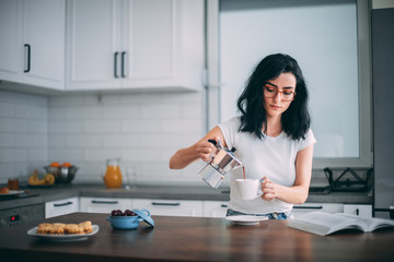 Beautiful young woman pouring coffee in the kitchen