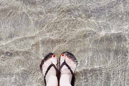 Feet in the water on the sand in flip-flops