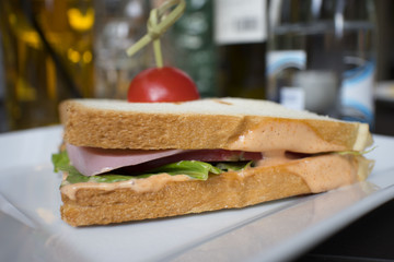 sandwich with cheese ham green tomato in a white plate on the table in the cafe on the background of drinks and food