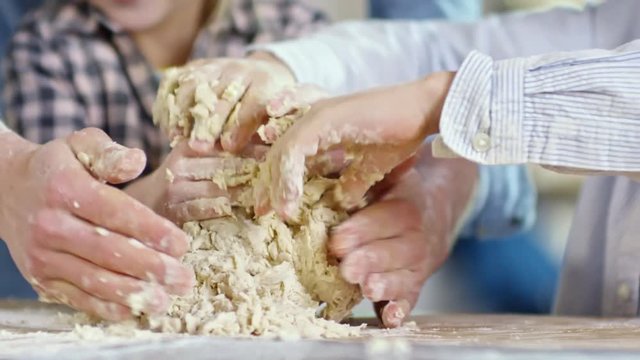 Close up hands of unrecognizable man and two children kneading dough on kitchen worktop