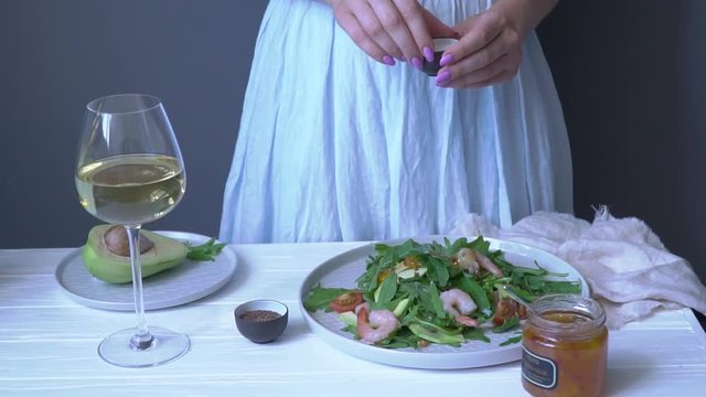 Woman sprinkles salt with arugula salad with shrimps and tomatoes, slow motion