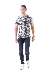 Cool confident handsome man in camouflage t-shirt walking towards camera and looking away. Full...