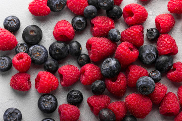 Fresh blueberries and raspberries on light concrete background, overhead view, close up