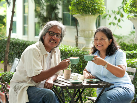 Senior couple laughing while drinking coffee in home garden.
