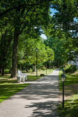 Stone pathway in the green park with bench and street lighting. Park of Saka manor. Estonia. Baltic.