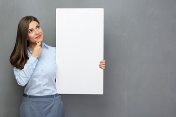 Thinking businesswoman holding white board looking up. Studio portrait with gray wall back.