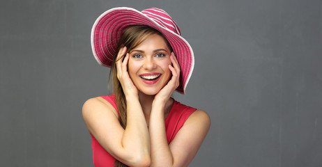 Smiling woman in red wearing big summer hat touching face.