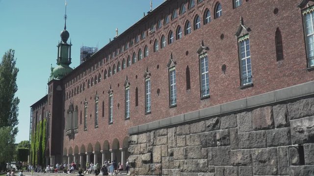 Sideview of City hall in Stockholm, Sweden. Showing the brick wall on the south side and people walking around the yard.