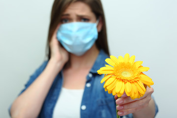 Young woman wearing medical mask holding yellow flower.