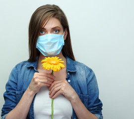 Woman wearing medical mask sniffs flower.
