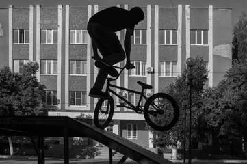 Silhouette of a young guy on BMX, doing a complicated trick in skatepark ramp. Extreme cycling...