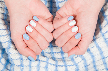 Closeup view of painted blue and white fingernails of young woman isolated on cozy warm blanket. Winter style of manicure. Horizontal color photography.