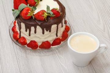 Homemade chocolate cake decorated with fresh strawberries on glass plate and cup of coffee