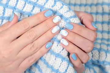 Closeup view of polished blue and white fingernails of young woman isolated on cozy warm blanket. Winter style of manicure. Horizontal color photography.