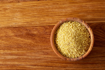 A wooden dish with millet on rustic wooden background, top view, close-up, selective focus.