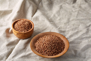 Bowl and plate full of buckwheat grains on homespun tablecloth, close-up, selective focus, shallow depth of field.