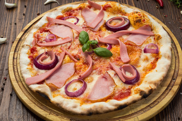 Delicious italian pizza with ham, sausages and onion decorated by basil leaves on wooden background