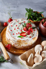 Strawberry tart covered with whipped sour cream surrounded by organic ingredients over white background, flat lay.