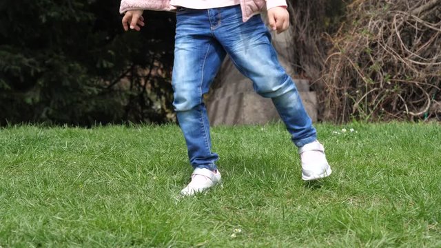 Child girl daughter legs in jeans jump dance on a green lawn grass in a park