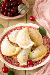 Pies with cherries, sprinkled with powdered sugar and berries of fresh cherries on a wooden surface.