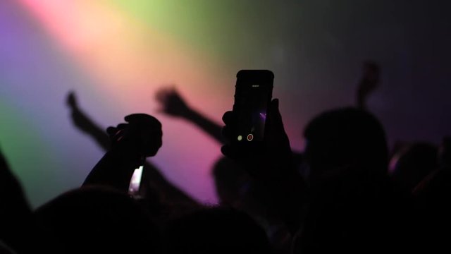 Mobile phone shooting a music concert by spectator silhouette hands in a stage lights