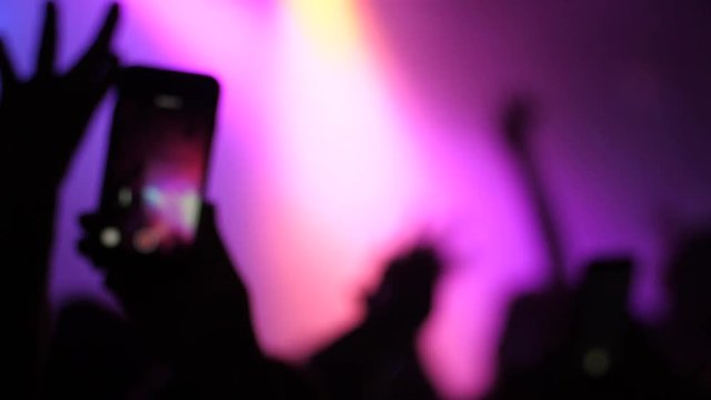 Mobile phone shooting a music concert by spectator silhouette hands in a stage lights
