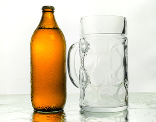 A bottle of beer, still closed and full, and a giant glass mug, over a mirror. White background.
