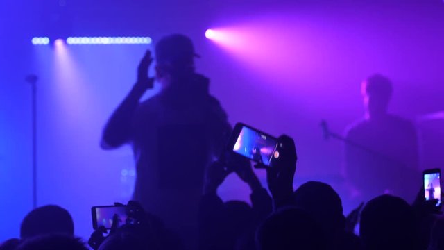 Spectators under concert stage shooting mobile phone video of performer singer