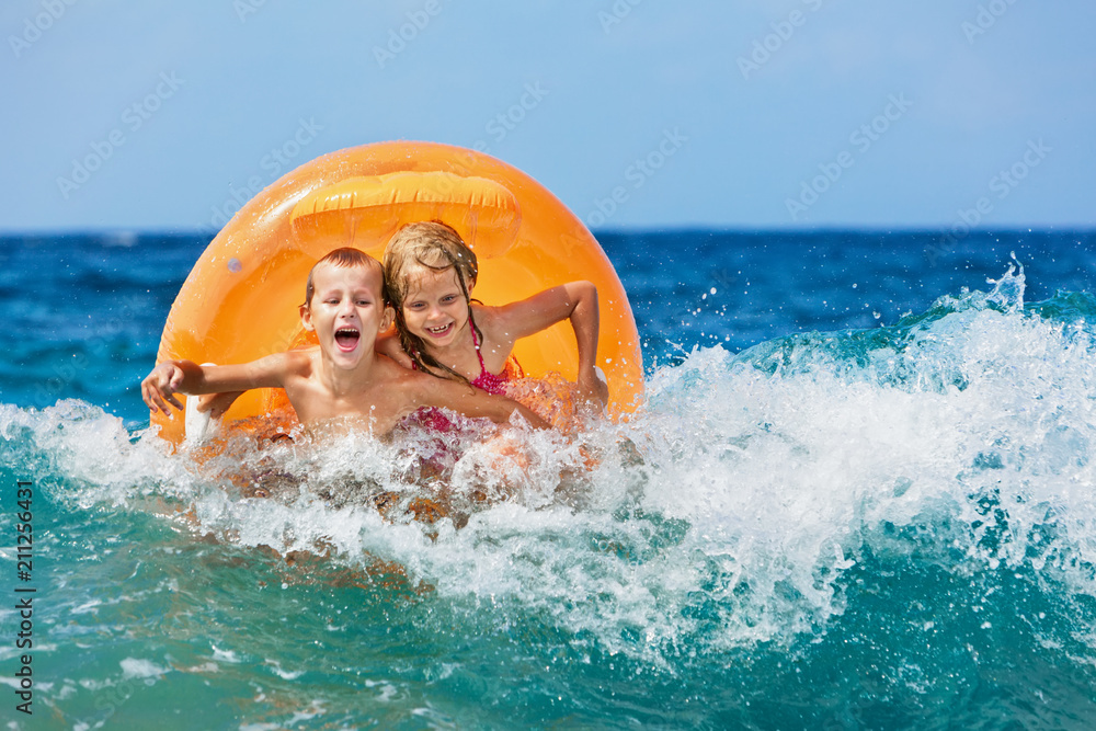 Wall mural happy kids have fun in sea surf on beach. joyful couple of children on inflatable ring ride on break