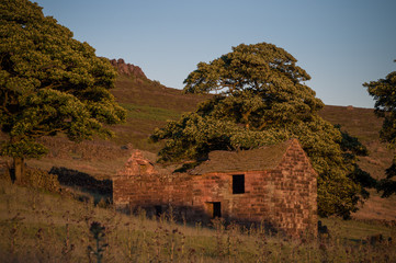Sunset lights the trees, heather, rocks and ruined barn at Roach End, The Roaches, Staffordshire in the Peak District National park.