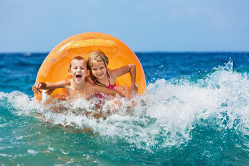 Happy kids have fun in sea surf on beach. Joyful couple of children on inflatable ring ride on...