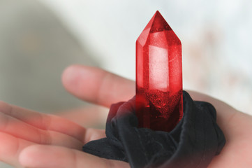 A large transparent mystical faceted crystal of colored red ruby, tourmaline on the palm on a light...