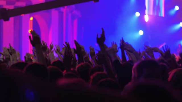 Handheld shot of insane and vigorous music fans dancing with hands up at the concert of favourite rock band