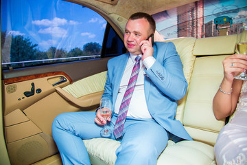 Stylish groom in  suit, communicate on mobile phone in luxury limousine