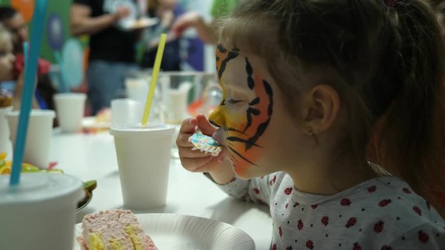 Body art painted face cute little girl on birthday theme party eating sweet cake