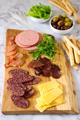 Appetizer table for wine or beer with sausages, dried meat and cheese, served with grissini, herbs and olives.