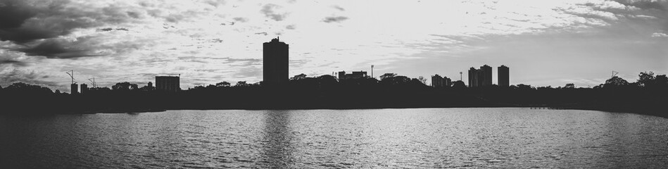 Silhouette of the lake and the city on the background on a cloudy day. Panoramic, black and white photo.