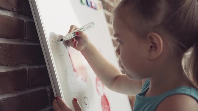Small little girl draws picture with marker on whiteboard. Closeup FullHD video.