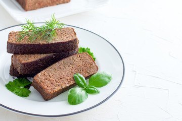Sliced pate-casserole from chicken liver on a white plate with fresh green, horizontal, copy space for text