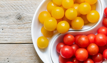 Yellow and red cherry tomatoes with water drops. Fresh and juicy organic vegetables in a white plate on a wooden table