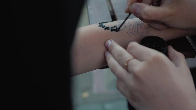 Drawing a child's tattoo on his hand with black paint. Beautiful drawing on a children's hand